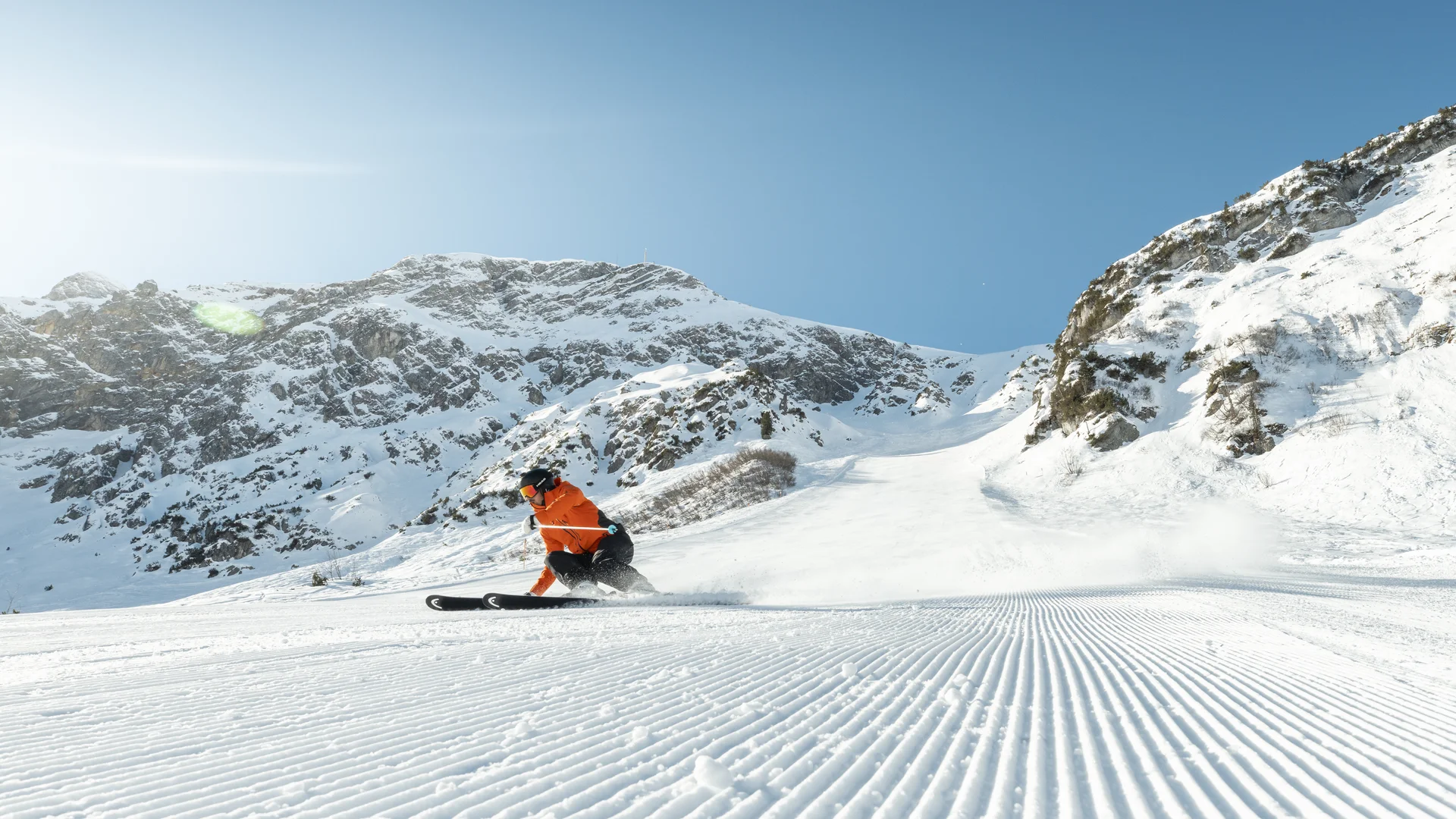 Hotel in Lech am Arlberg mit Ski-in/Ski-out | Hotel Panorama Skifahrer in orangefarbener Jacke fährt eine präparierte Piste vor schneebedeckten Bergen hinab