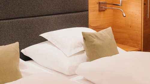 Hotel in Lech am Arlberg mit Ski-in/Ski-out | Hotel Panorama Hotelbett mit weißer Bettwäsche, beigem Zierkissen, gepolstertem Kopfteil und Wandlampe