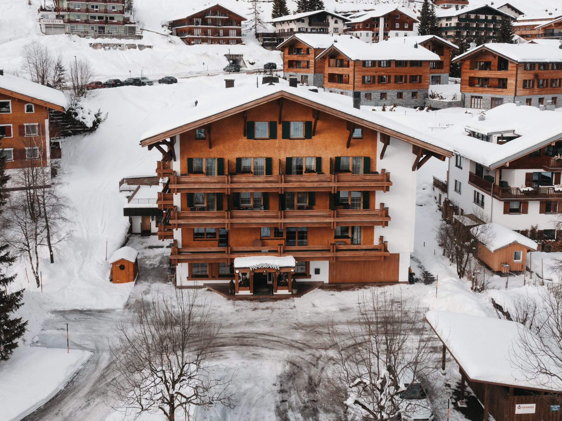 Hotel in Lech am Arlberg mit Ski-in/Ski-out | Hotel Panorama Holzchalet mit Balkonen in einem verschneiten Bergdorf, umgeben von weiteren Häusern