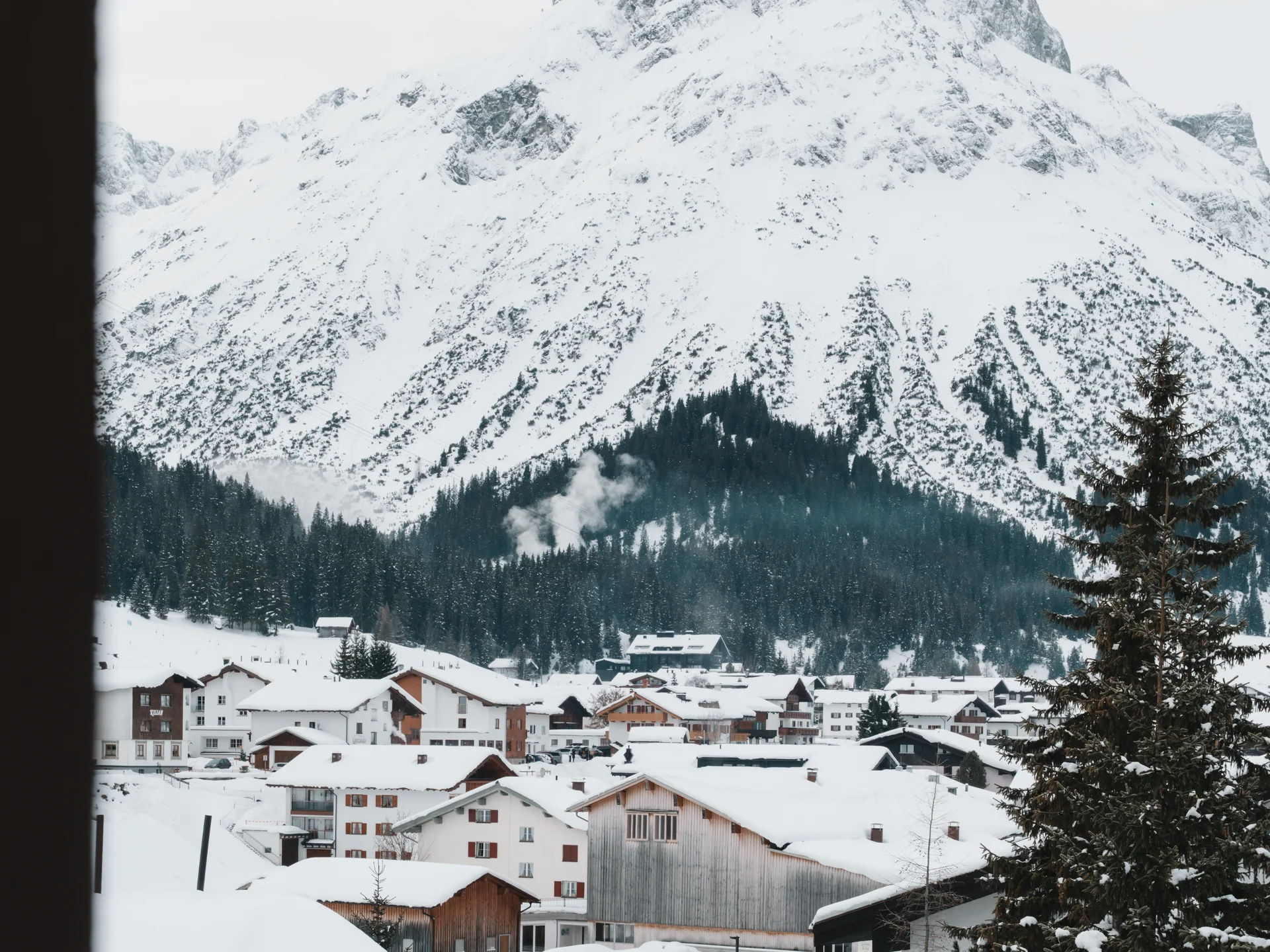 Hotel in Lech am Arlberg mit Ski-in/Ski-out | Hotel Panorama Verschneites Bergdorf vor einem hohen schneebedeckten Berg, eingerahmt von einem Fenster